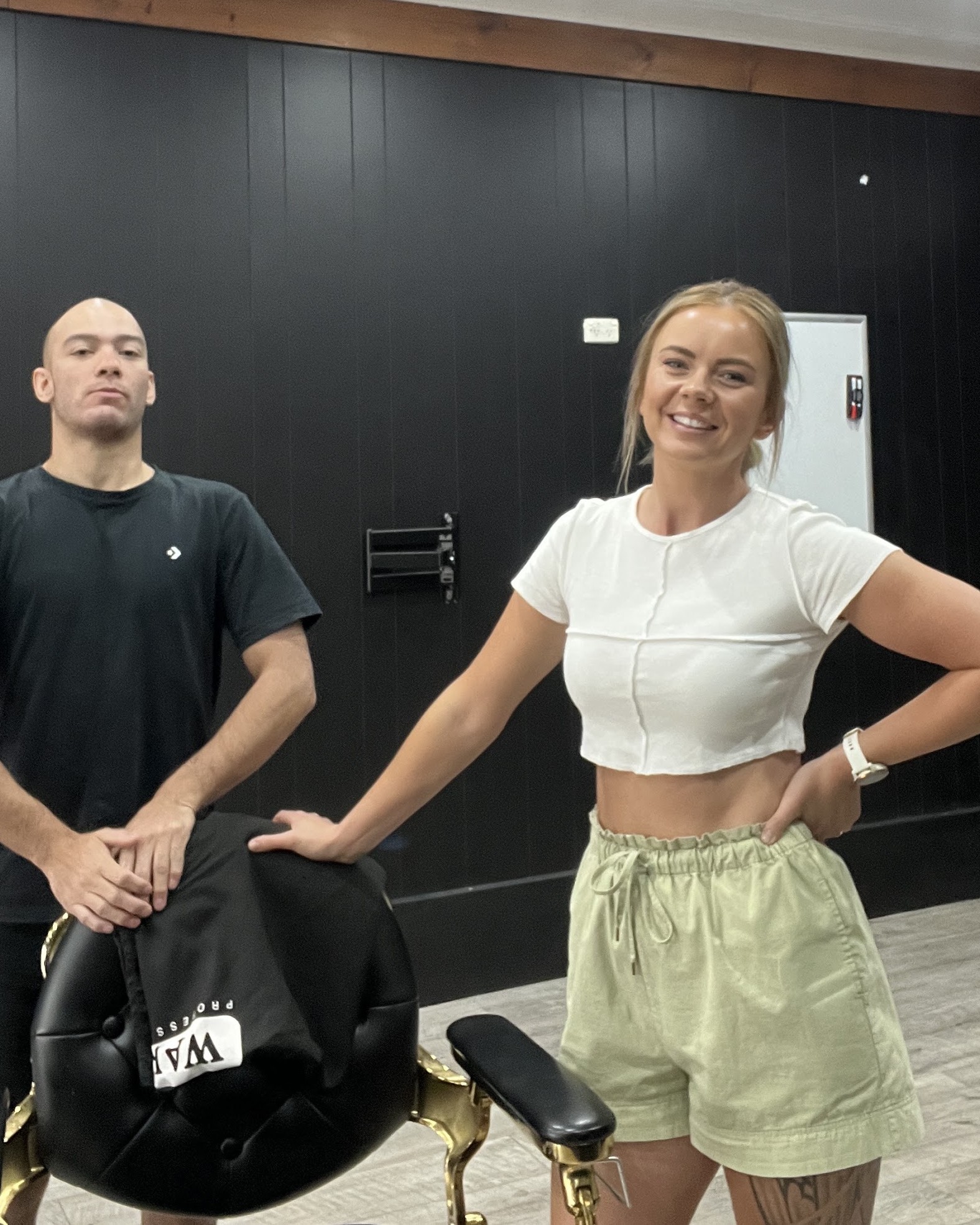 Two of the team beside the gold barber chair against the black shiplap wall