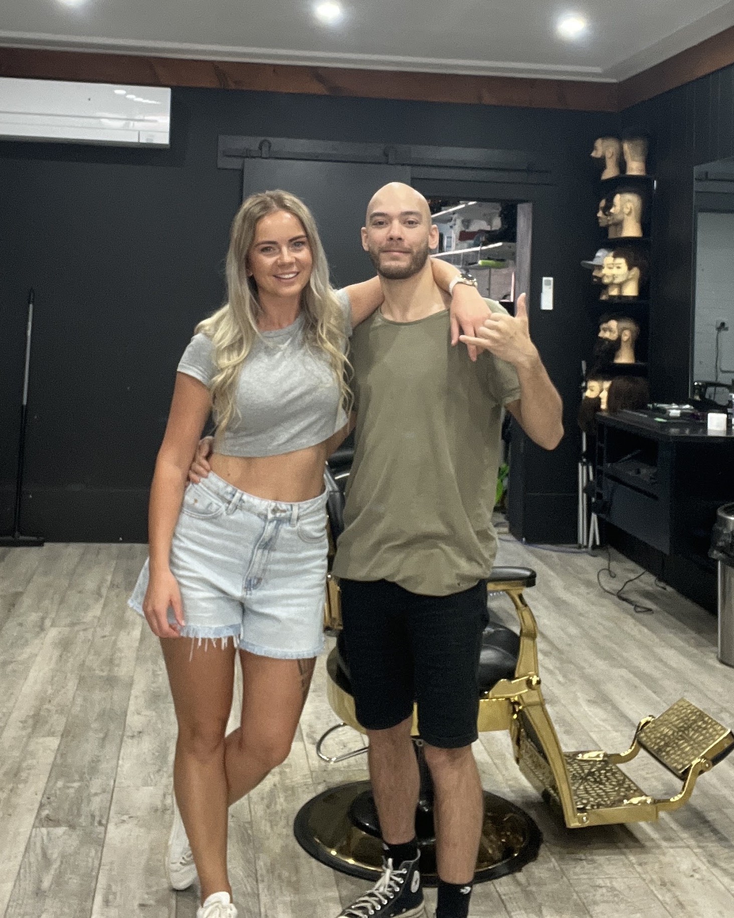 Two of the team beside the gold barber chair, practice heads on the shelves behind