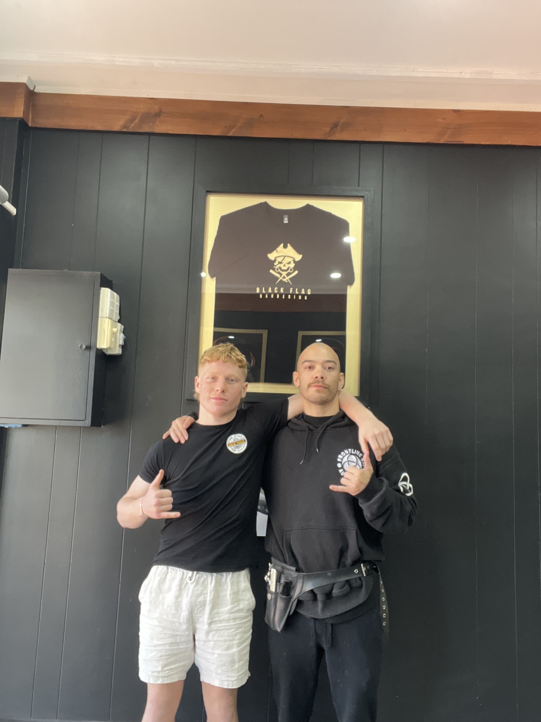 Two barbers in front of the framed Black Flag shirt on the shop wall