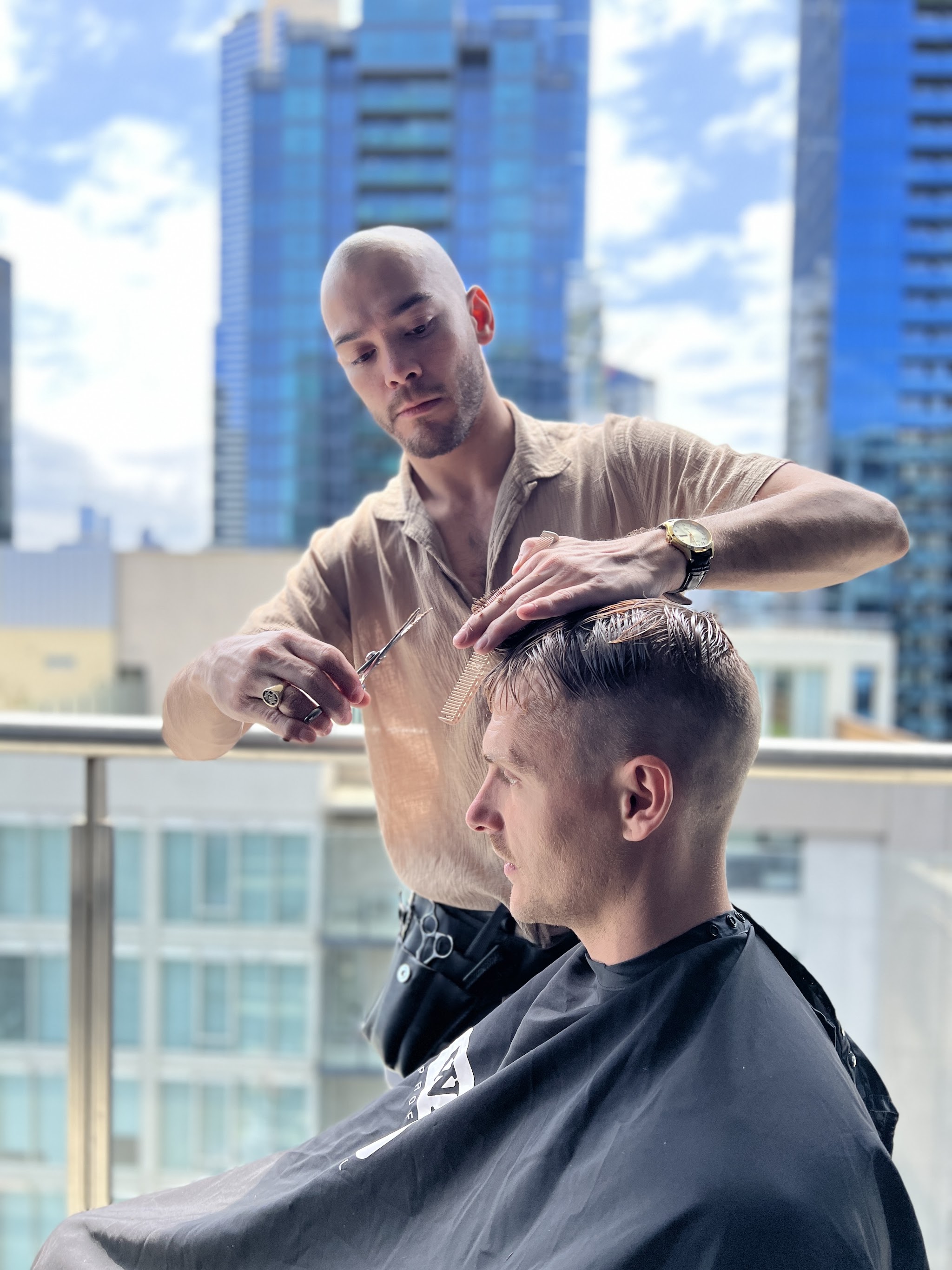 Bart cutting a client's hair with scissors and comb, city skyline behind