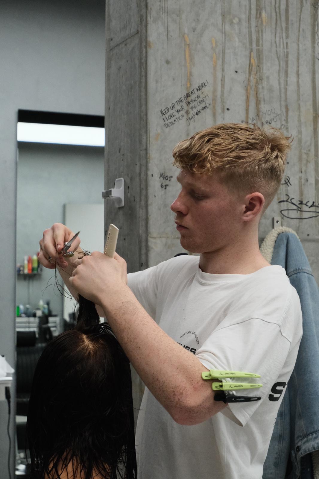 A barber scissor cutting at an education session, signed messages on the concrete wall behind